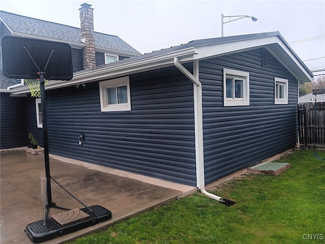 view of property exterior with a yard, a patio, a chimney, and fence