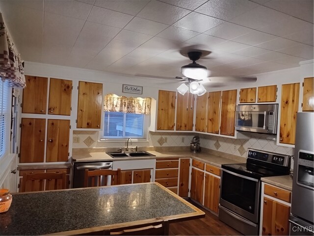 kitchen featuring brown cabinets, stainless steel appliances, tasteful backsplash, a sink, and ceiling fan