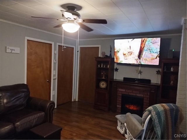 living area with a brick fireplace, a ceiling fan, ornamental molding, and wood finished floors