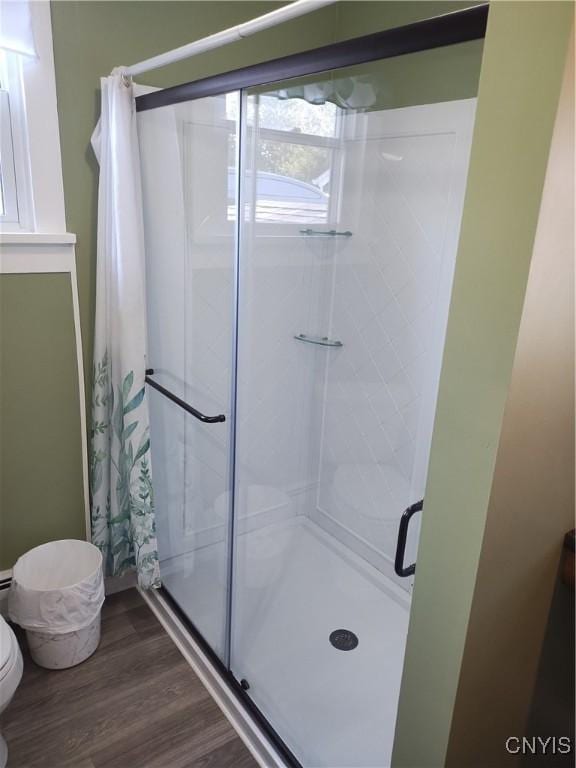 bathroom featuring wood finished floors, toilet, and a shower stall