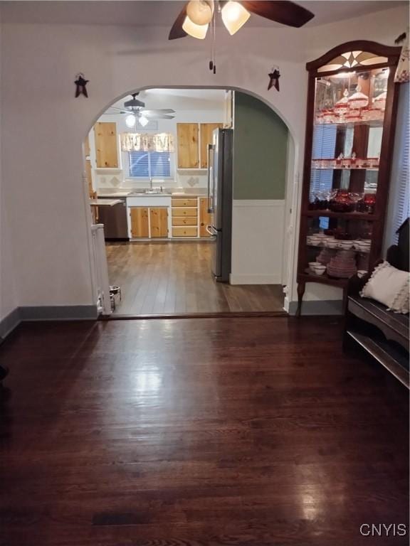 unfurnished living room with arched walkways, dark wood-style flooring, and a ceiling fan