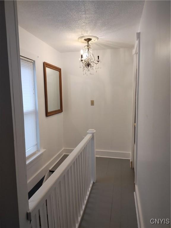 hallway featuring a textured ceiling, baseboards, an upstairs landing, and a notable chandelier