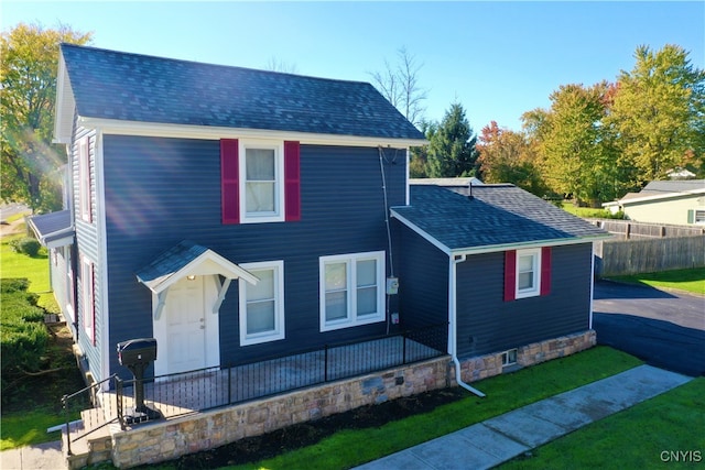 view of front facade featuring a front yard, roof with shingles, and fence