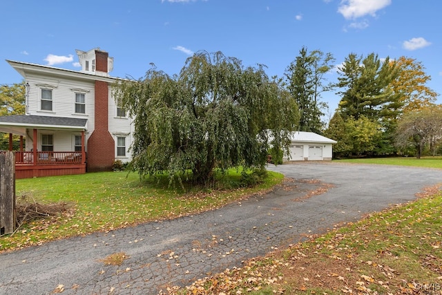 view of property exterior with covered porch, a yard, a garage, and an outbuilding