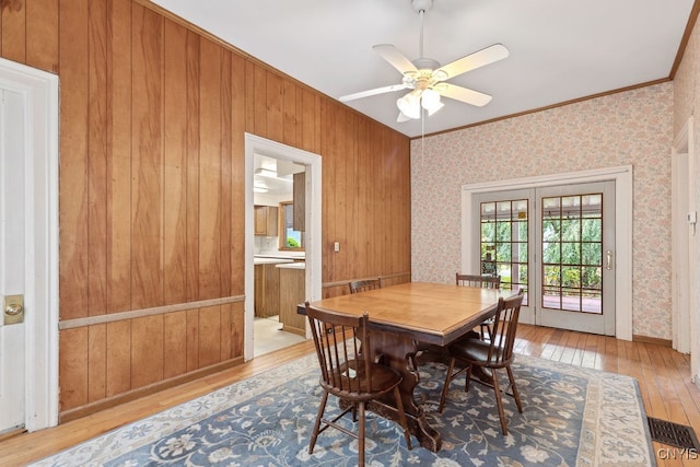 dining room featuring ornamental molding, wood walls, light wood-type flooring, and ceiling fan