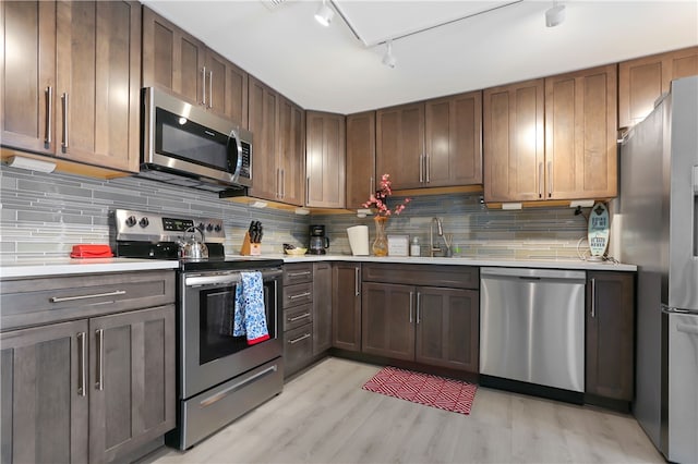 kitchen with decorative backsplash, track lighting, sink, appliances with stainless steel finishes, and light hardwood / wood-style floors