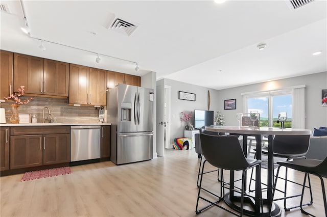 kitchen with decorative backsplash, track lighting, appliances with stainless steel finishes, light hardwood / wood-style floors, and sink