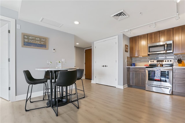 kitchen with track lighting, light hardwood / wood-style floors, stainless steel appliances, decorative backsplash, and a breakfast bar area