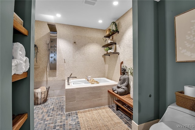 bathroom with tile patterned floors, a relaxing tiled tub, and toilet