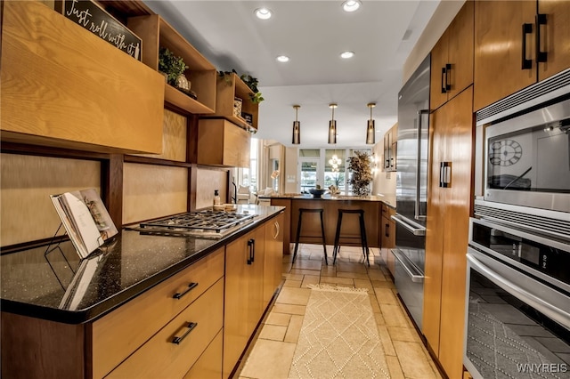 kitchen with built in appliances, dark stone counters, and kitchen peninsula