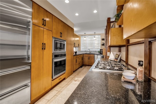 kitchen featuring built in appliances, sink, dark stone counters, and decorative light fixtures