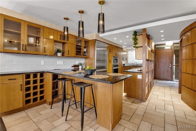 kitchen featuring tasteful backsplash, kitchen peninsula, stainless steel built in refrigerator, decorative light fixtures, and a breakfast bar