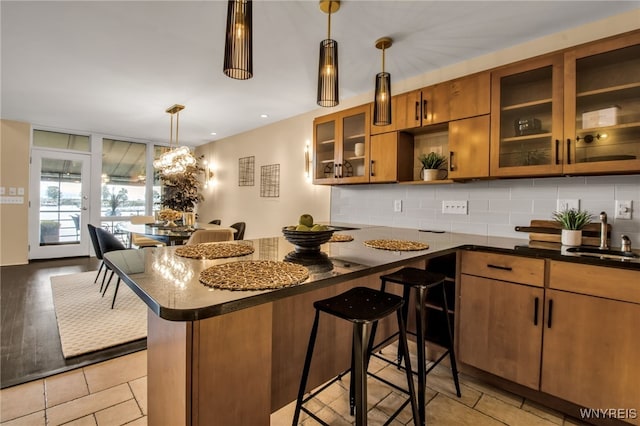 kitchen featuring a kitchen breakfast bar, light hardwood / wood-style flooring, hanging light fixtures, backsplash, and sink