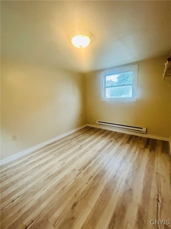 unfurnished room with baseboard heating and light wood-type flooring