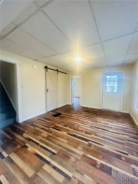 basement featuring a barn door, wood-type flooring, and a paneled ceiling