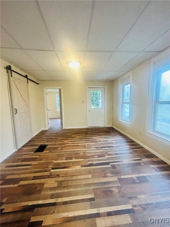 empty room featuring dark hardwood / wood-style flooring, a drop ceiling, and a barn door