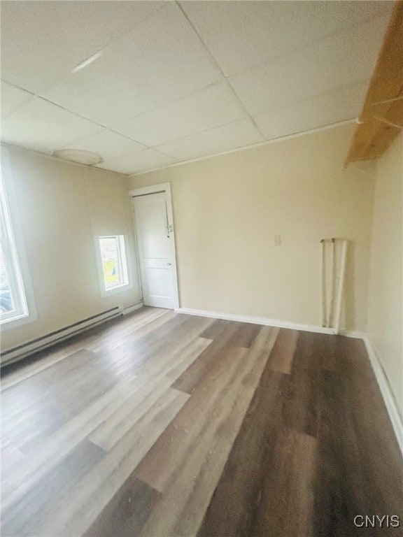 empty room with a paneled ceiling, a baseboard heating unit, and hardwood / wood-style floors