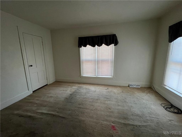 unfurnished bedroom with carpet floors, multiple windows, visible vents, and baseboards