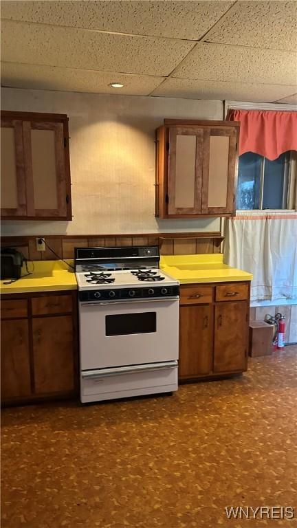 kitchen with brown cabinets, white range with gas stovetop, light countertops, and dark floors