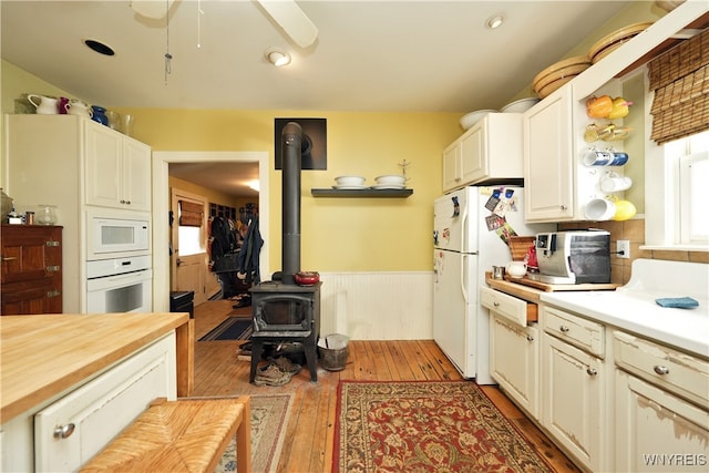 kitchen featuring a wood stove, butcher block countertops, white appliances, white cabinets, and light wood-type flooring