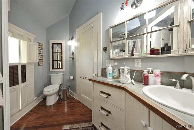 bathroom featuring wood-type flooring, vanity, toilet, and lofted ceiling