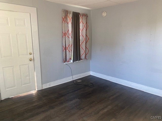 spare room featuring a drop ceiling and dark wood-type flooring