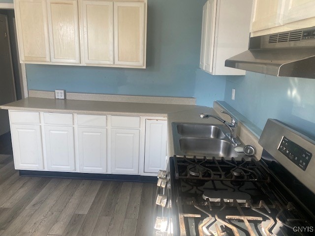 kitchen featuring dark hardwood / wood-style flooring, white cabinetry, stainless steel gas stove, range hood, and sink