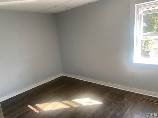 empty room with a drop ceiling and dark hardwood / wood-style flooring