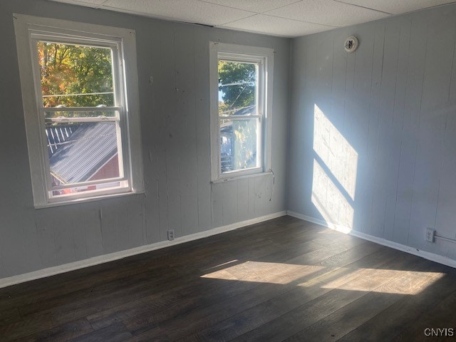 empty room with a drop ceiling, dark hardwood / wood-style floors, and wooden walls