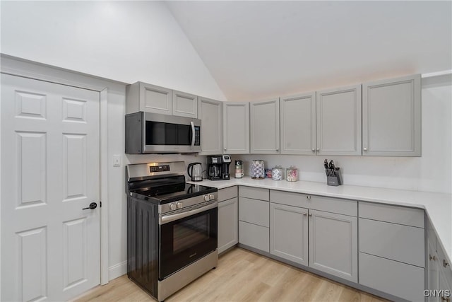 kitchen featuring stainless steel appliances, light hardwood / wood-style flooring, lofted ceiling, and gray cabinetry