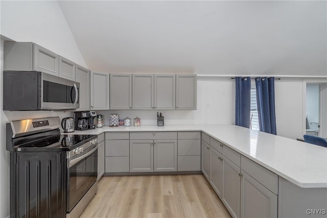 kitchen with vaulted ceiling, gray cabinets, light wood-type flooring, appliances with stainless steel finishes, and kitchen peninsula