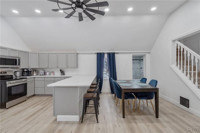 kitchen with gray cabinetry, a kitchen breakfast bar, vaulted ceiling, light wood-type flooring, and appliances with stainless steel finishes