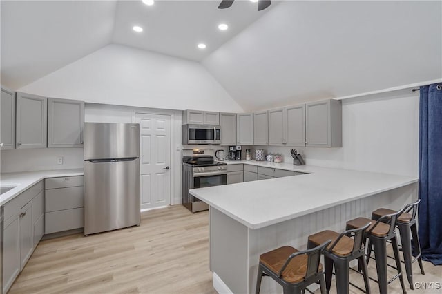 kitchen with kitchen peninsula, appliances with stainless steel finishes, a kitchen breakfast bar, gray cabinetry, and light hardwood / wood-style flooring