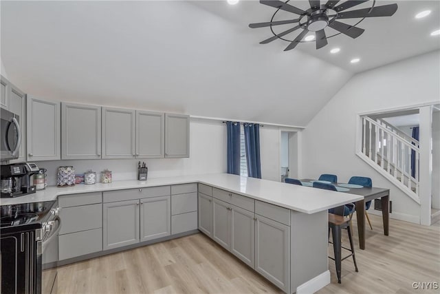 kitchen with kitchen peninsula, gray cabinetry, vaulted ceiling, light hardwood / wood-style floors, and a breakfast bar area