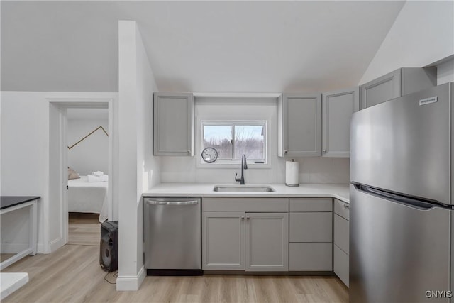 kitchen featuring appliances with stainless steel finishes, gray cabinetry, sink, light hardwood / wood-style flooring, and lofted ceiling