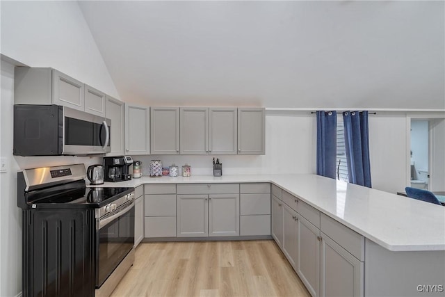 kitchen featuring kitchen peninsula, appliances with stainless steel finishes, gray cabinetry, vaulted ceiling, and light hardwood / wood-style floors