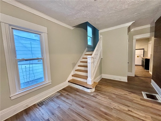 staircase featuring crown molding, wood-type flooring, and a textured ceiling