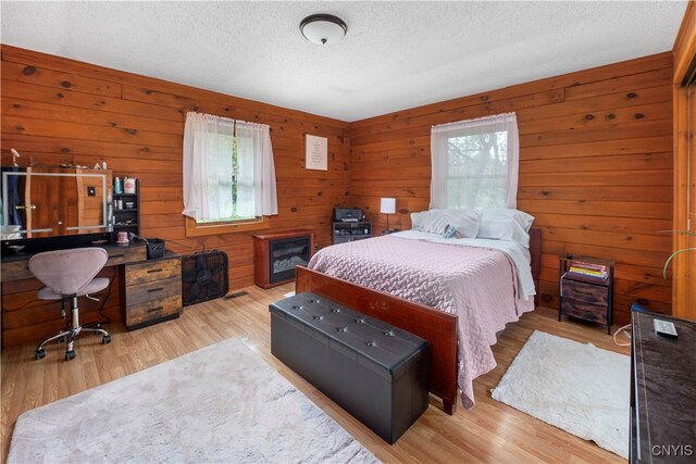 bedroom with wooden walls, multiple windows, and light hardwood / wood-style floors