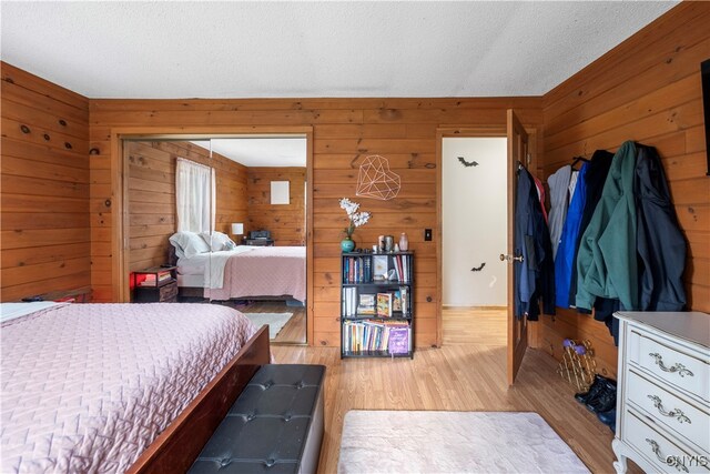 bedroom featuring a textured ceiling, light hardwood / wood-style flooring, and wooden walls