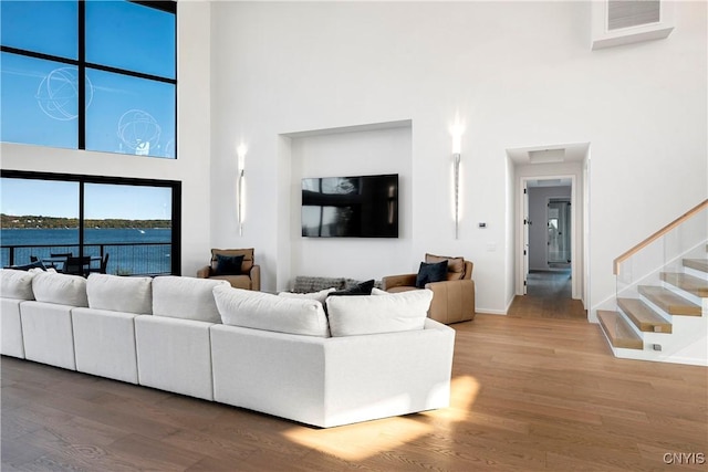 living area with stairs, wood finished floors, baseboards, visible vents, and a towering ceiling