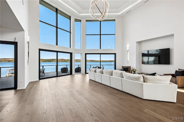 unfurnished living room featuring a high ceiling, hardwood / wood-style flooring, plenty of natural light, a raised ceiling, and a water view