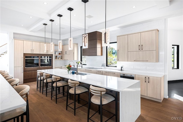 kitchen with a kitchen island with sink, light brown cabinets, a breakfast bar area, hanging light fixtures, and sink