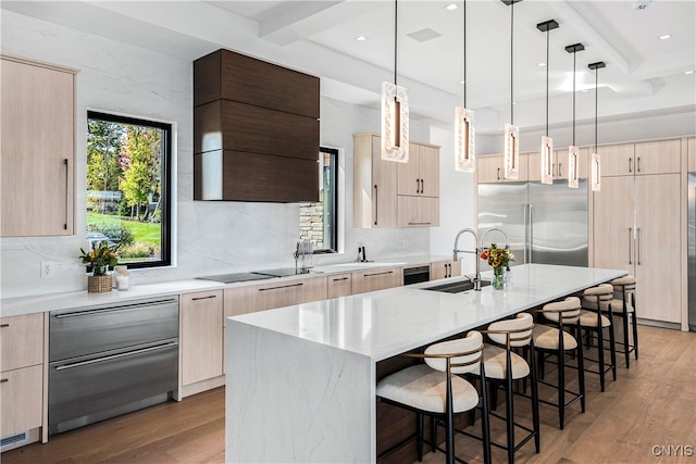 kitchen with sink, an island with sink, light hardwood / wood-style floors, high quality fridge, and beam ceiling