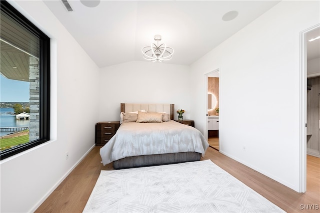 bedroom with ensuite bathroom, an inviting chandelier, vaulted ceiling, and light hardwood / wood-style floors