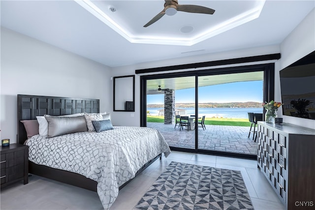 tiled bedroom with a raised ceiling, a water view, access to outside, and ceiling fan