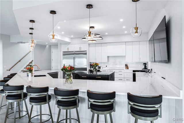 kitchen with a large island, hanging light fixtures, a breakfast bar area, white cabinetry, and built in refrigerator