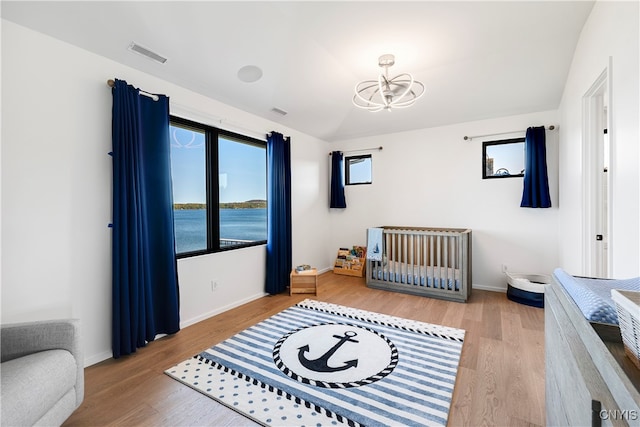 bedroom featuring hardwood / wood-style floors, a notable chandelier, and a water view