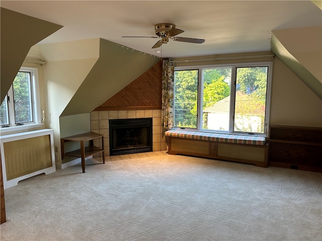 bonus room with wood walls, lofted ceiling, a tiled fireplace, light carpet, and ceiling fan