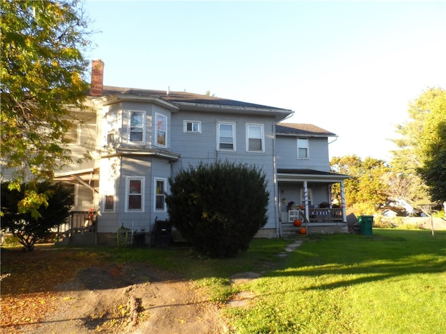 rear view of house featuring covered porch and a lawn