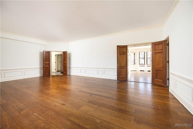 unfurnished room featuring dark wood-style floors, wainscoting, crown molding, and a decorative wall